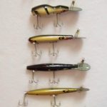 This is an array of 6 Devels Horse Rooters. 1. Snake Head in in un-cataloged color - Yellow w/Black Spots; 2. Razorback Rooter in White w/Black Stripes; 3. S-400 Devels Horse Rooter in un-cataloged color - Yellow/Gold Scale w/Black Back; 4. Un-cataloged lure and color - Devels Horse Rooter using F-100 body and rear hook on the belly - color Black w/Spots in Red, Green, White; 5. Un-cataloged lure in Shad. Devels Horse Rooter using F-100 body with rear hook coming directly out the back; 6. Un-cataloged lure and color. Devels Horse Rooter using F-200 body in Yellow w/Black Spots. The only lure missing from this array is the Well Digger which was the first of the Rooter line.