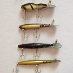 This is an array of 6 Devels Horse Rooters. 1. Snake Head in in un-cataloged color - Yellow w/Black Spots; 2. Razorback Rooter in White w/Black Stripes; 3. S-400 Devels Horse Rooter in un-cataloged color - Yellow/Gold Scale w/Black Back; 4. Un-cataloged lure and color - Devels Horse Rooter using F-100 body and rear hook on the belly - color Black w/Spots in Red, Green, White; 5. Un-cataloged lure in Shad. Devels Horse Rooter using F-100 body with rear hook coming directly out the back; 6. Un-cataloged lure and color. Devels Horse Rooter using F-200 body in Yellow w/Black Spots. The only lure missing from this array is the Well Digger which was the first of the Rooter line.