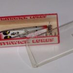 C-900 Pa Scooter - Devils Horse.
This lure is in a one piece box with the flexible plastic top. The box is stamped C-913 Devils Horse PA Scooter. Color #13 Silver Shiner. The Pa Scooter has a 4" wood body which is flat on the bottom. It has one small rounded spinner on the rear. It has two hooks.